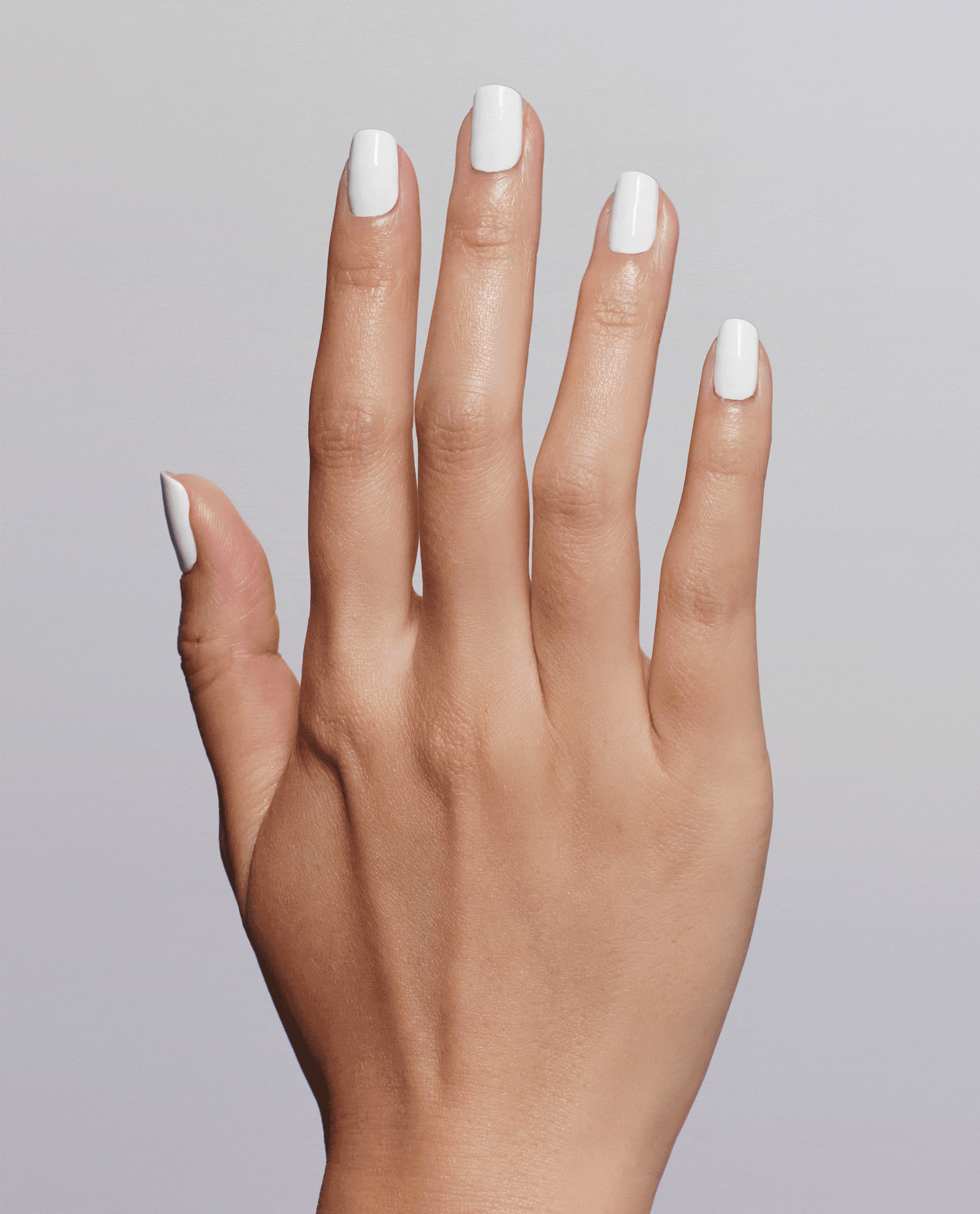 Hand displays a glossy white manicure using OPI Nail Envy Alpine Snow Nail Strengthener, a trending nail treatment, against a soft gray studio background.