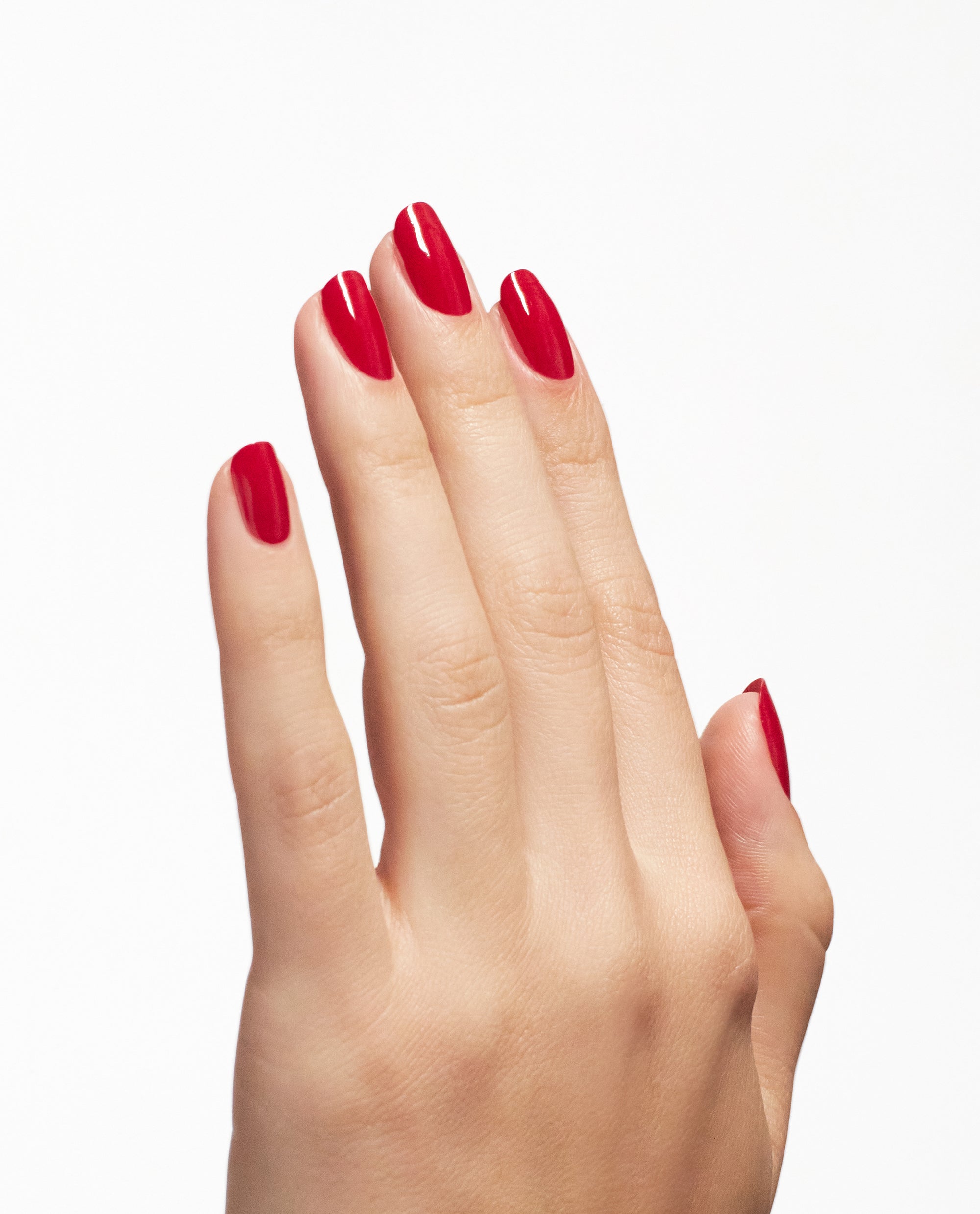 Manicured hand shows glossy OPI Nail Envy Big Apple Red nail strengthener on rounded nails, highlighting a bold red shade for fall nail colors against a white background.