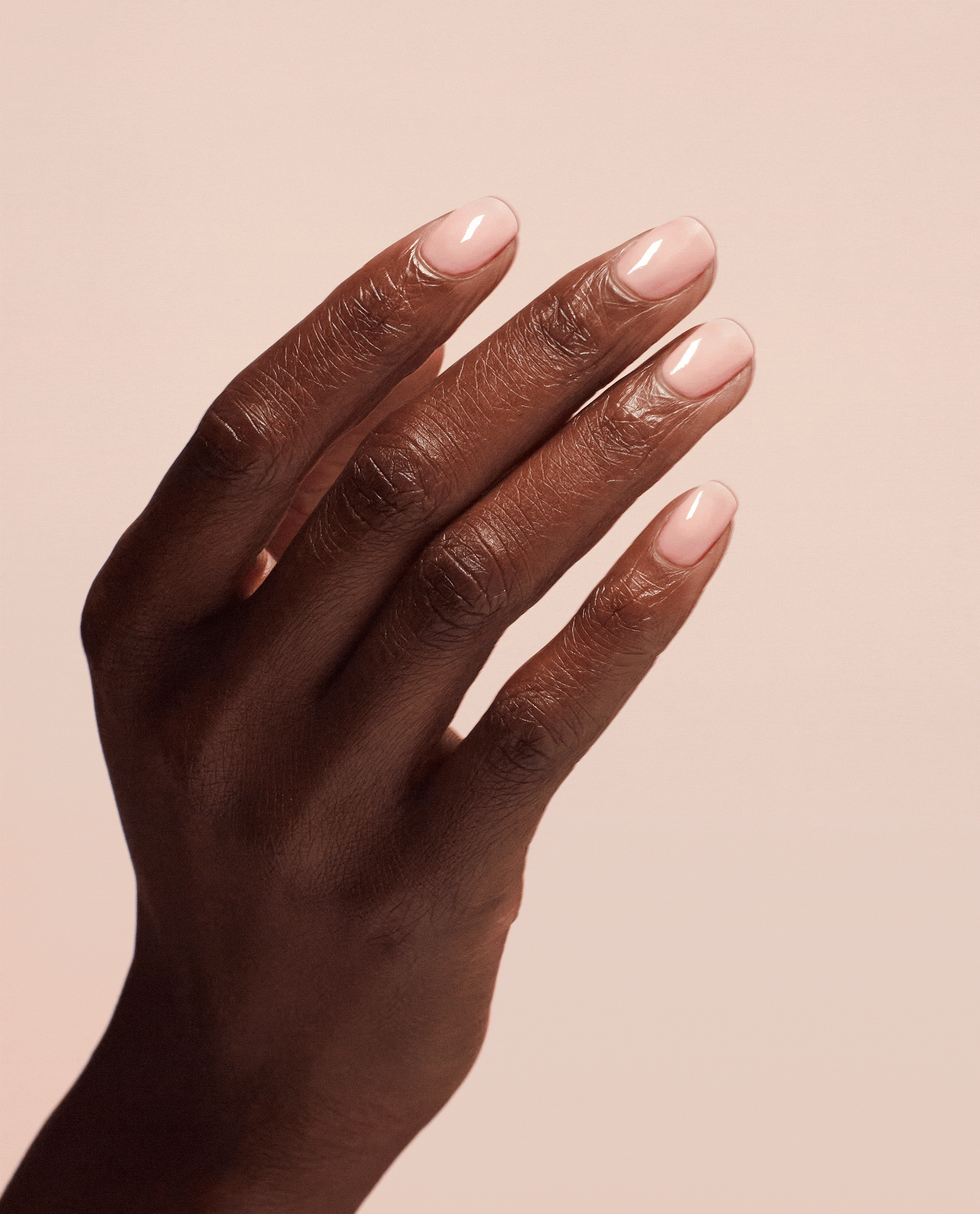 Hand with short, glossy nude-pink nails flexing to show the smooth, strengthened finish created by OPI Nail Envy Bubble Bath Nail Strengthener treatment, ideal as a nail polish gift set option against a soft blush background.