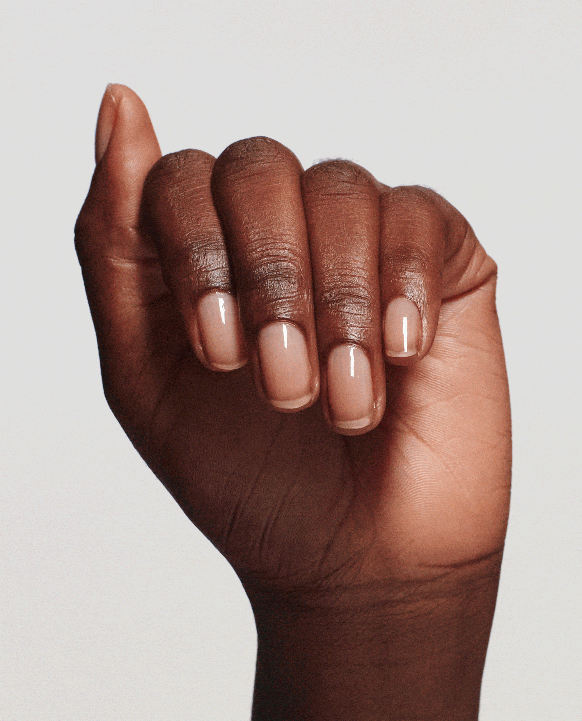 Hand with neatly manicured, glossy natural nails flexing to show strengthened tips after applying Nail Envy® Nail Strengthener by OPI, a clear treatments and strengtheners formula ideal for an OPI nail polish gift set promo on a clean studio background.