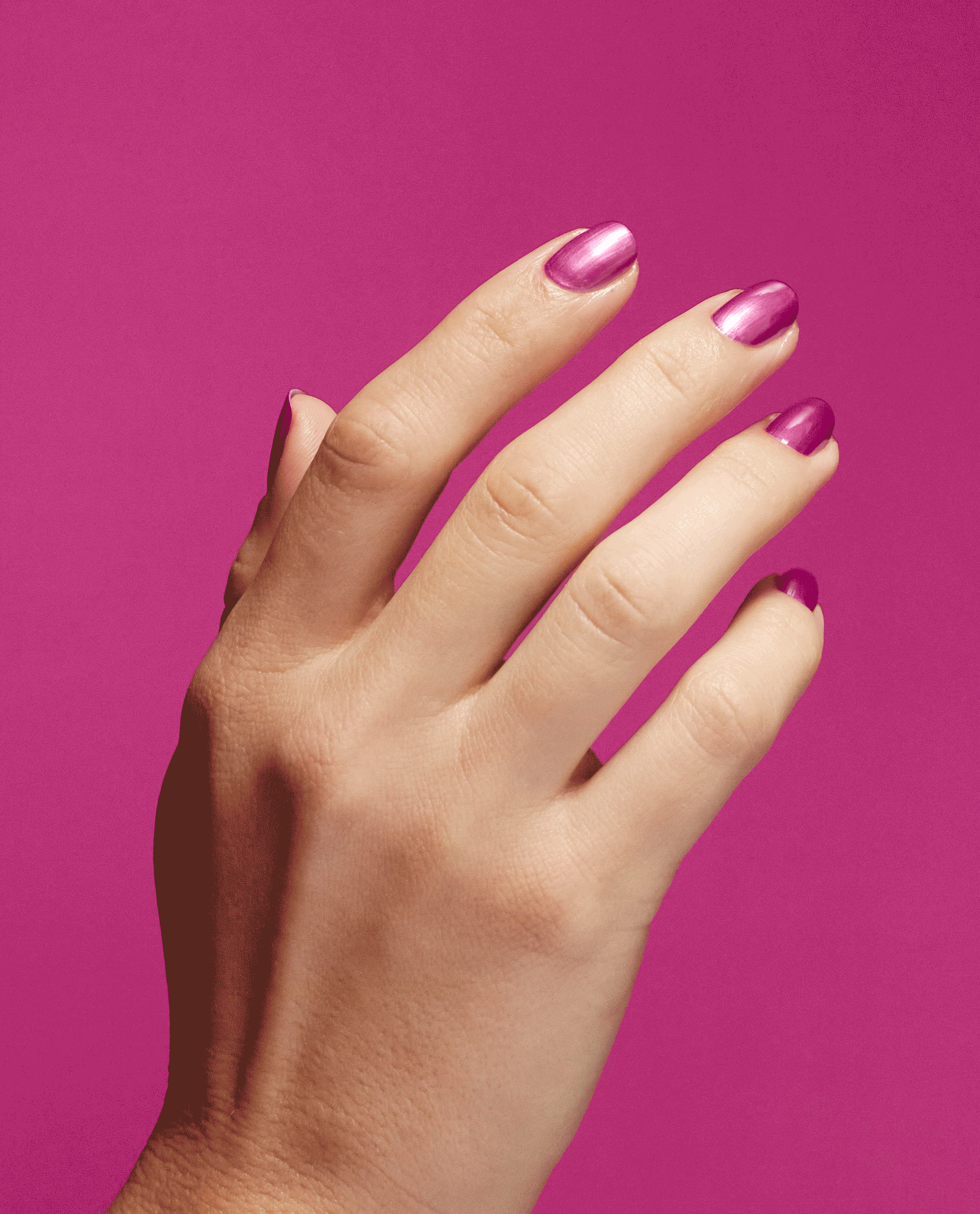 Hand displays glossy metallic pink nails with OPI Nail Envy Powerful Pink Nail Strengthener, a trending nail treatment, against a vivid magenta background.