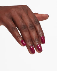 Hand displays a glossy berry manicure using OPI Nail Envy Tough Luv Nail Strengthener, a rich fall nail color on short rounded-square nails against a clean white background.