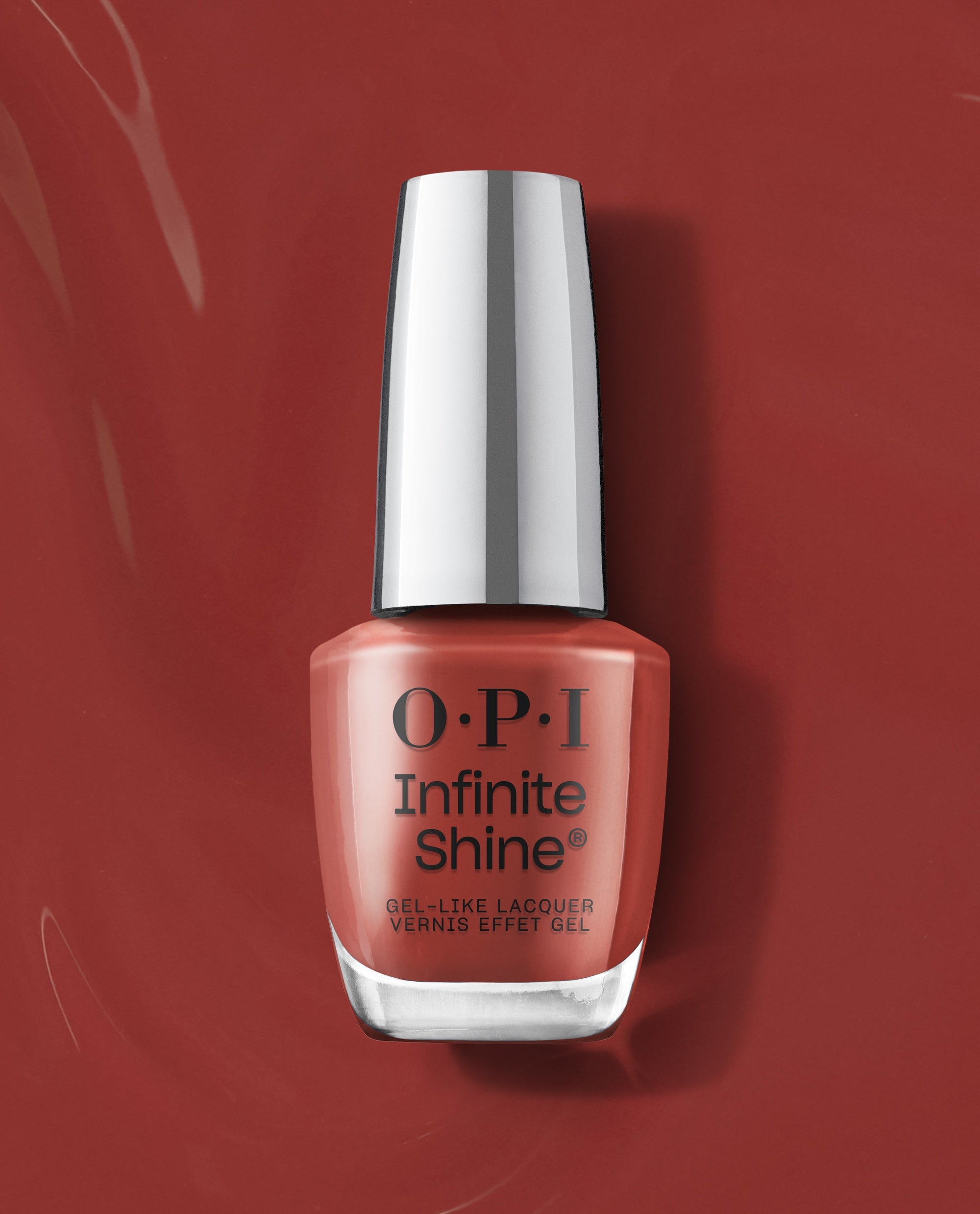 OPI Infinite Shine Nail Prep Rally gel-like lacquer bottle stands upright on a glossy terracotta red background, showcasing a warm coral shade for fall nail colors.
