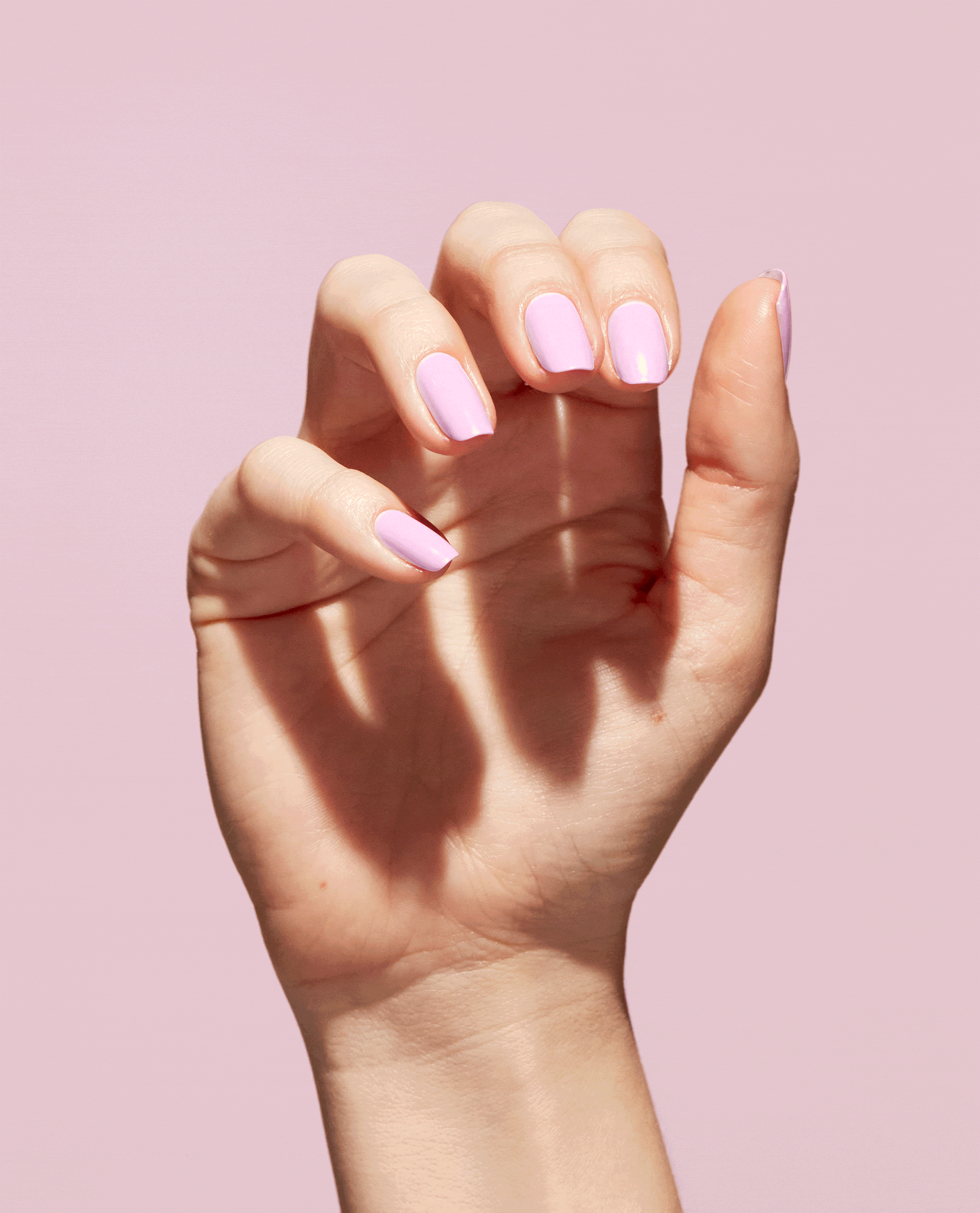 Hand displays glossy pastel mauve-pink nails painted with OPI Natural Mauvement Nature Strong vegan nail lacquer, a soft pick for fall nail colors, against a pale pink background.