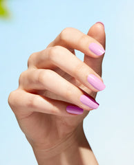 Hand displays glossy pink-lavender nails in OPI Natural Mauvement Nature Strong Vegan Nail Lacquer, a soft mauve option for fall nail colors, against a bright pale blue background.