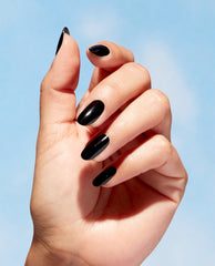 Hand modeling glossy black almond nails painted with OPI Onyx Skies Nature Strong Vegan Nail Lacquer, a trending manicure shade, against a bright blue sky.