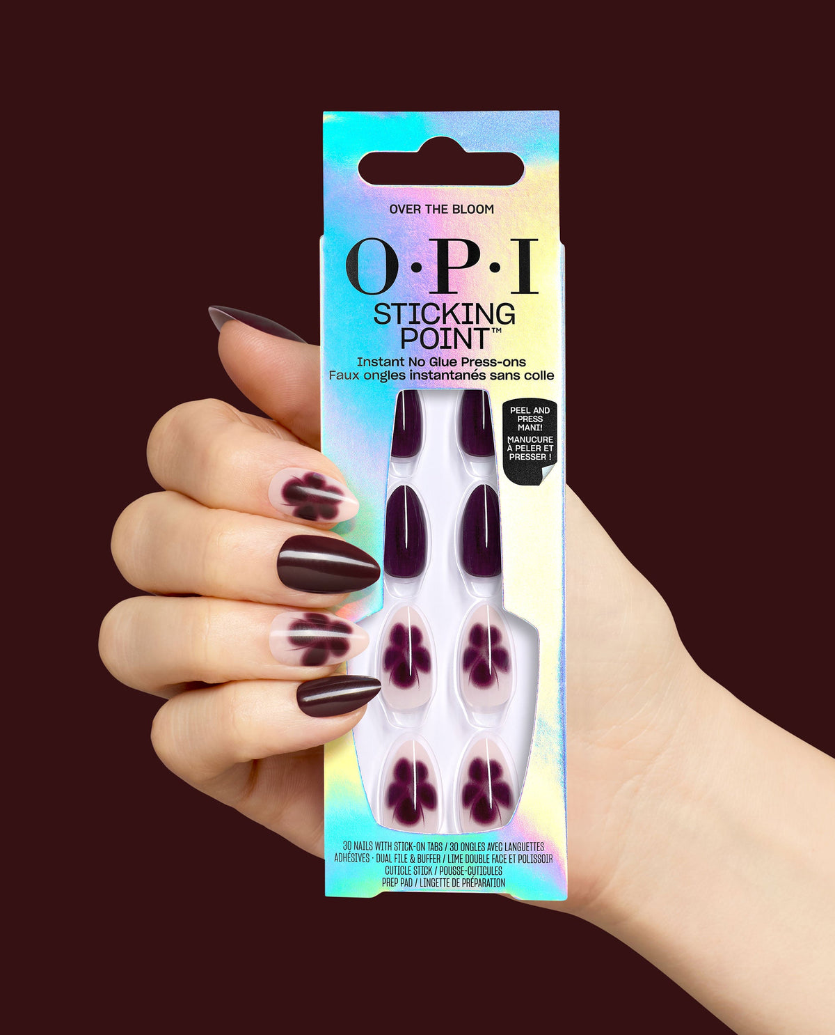 Over the Bloom OPI Sticking Point press-on nails are held in hand, showing glossy deep plum and sheer floral nail designs in iridescent packaging against a dark burgundy background, ideal for fall nail colors.