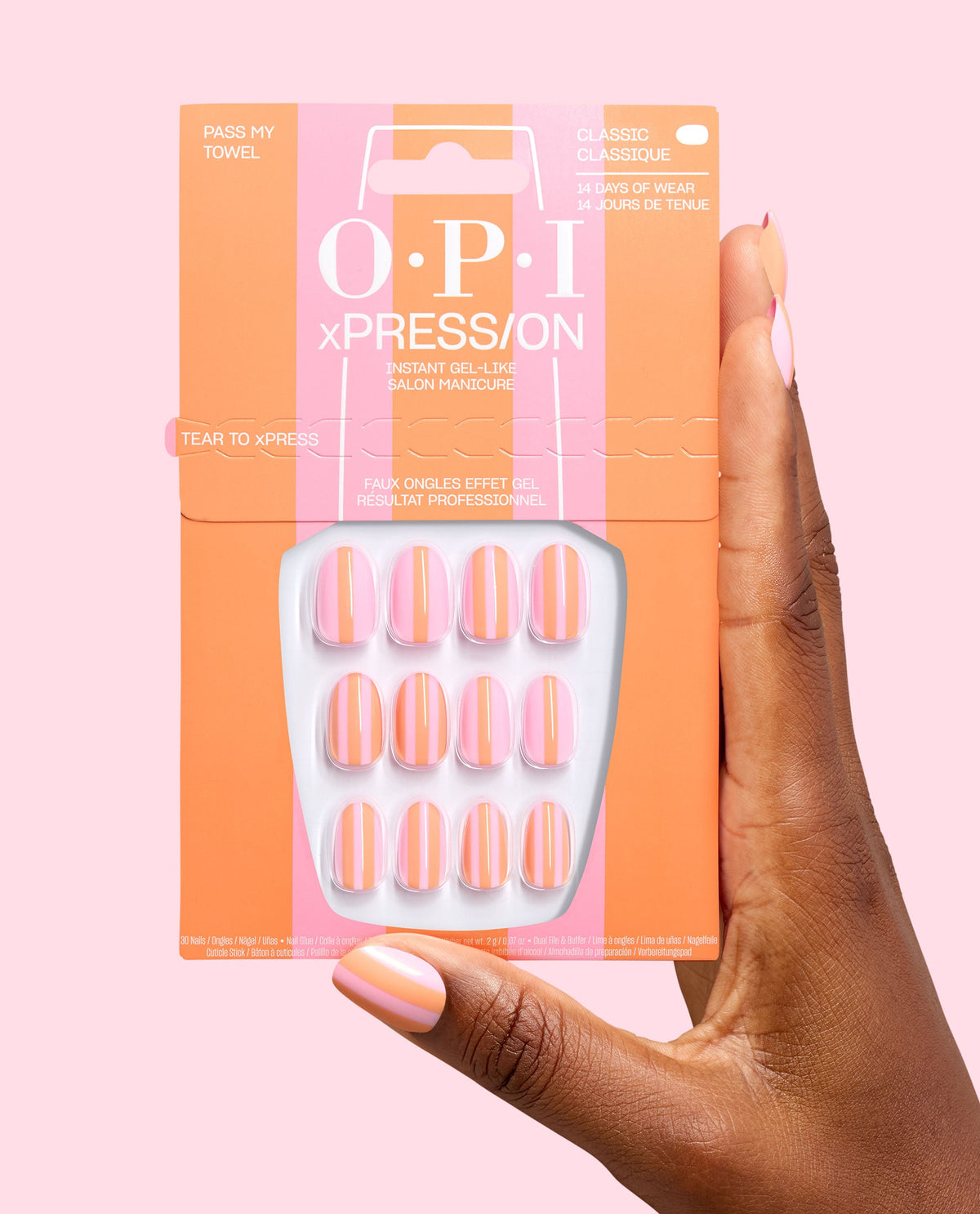 OPI xPRESS/ON Pass my Towel press-on nails in a trending pink and orange striped design, held in matching packaging by a hand with the manicure on a pale pink background.