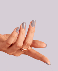 Hand with long square-shaped nails painted in Peace of Mined, a soft gray-purple OPI nail polish nail lacquer, gracefully posed against a pale lavender background with a gold ring accenting the minimalist manicure.