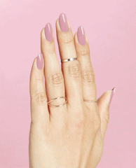 Hand with long oval nails painted in (P)Ink on Canvas, a glossy mauve-pink OPI nail polish, resting against a solid pink background and styled with delicate gold and silver rings to showcase the nail lacquer color and shine.