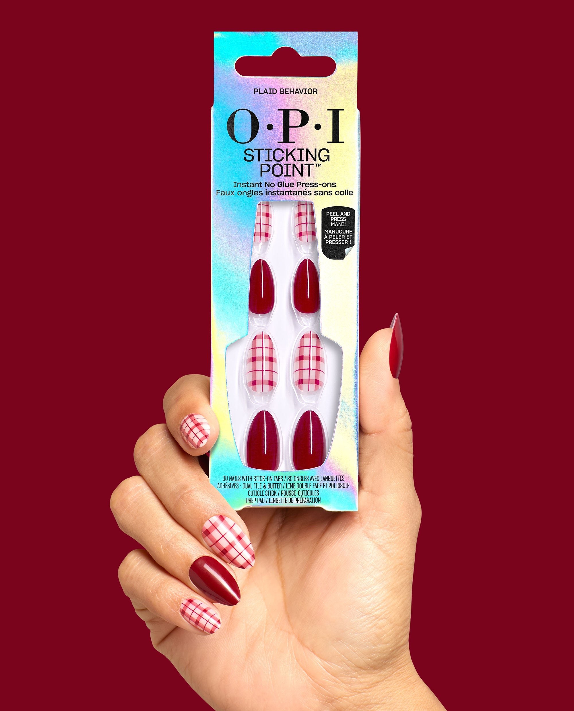 Hand holding OPI Sticking Point Plaid Behavior press-on nails with glossy deep red and pink plaid designs, showcasing fall nail colors against a burgundy background.