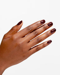 Hand modeling glossy deep raisin-burgundy OPI Infinite Shine Raisin' The Bar nail polish, a rich choice for fall nail colors, on a clean white background.