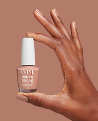 Hand with glossy nude-pink nails holds OPI Nature Strong Vegan Nail Lacquer in Rooting For Hue, a trending vegan nail polish shade, against a warm mauve background.