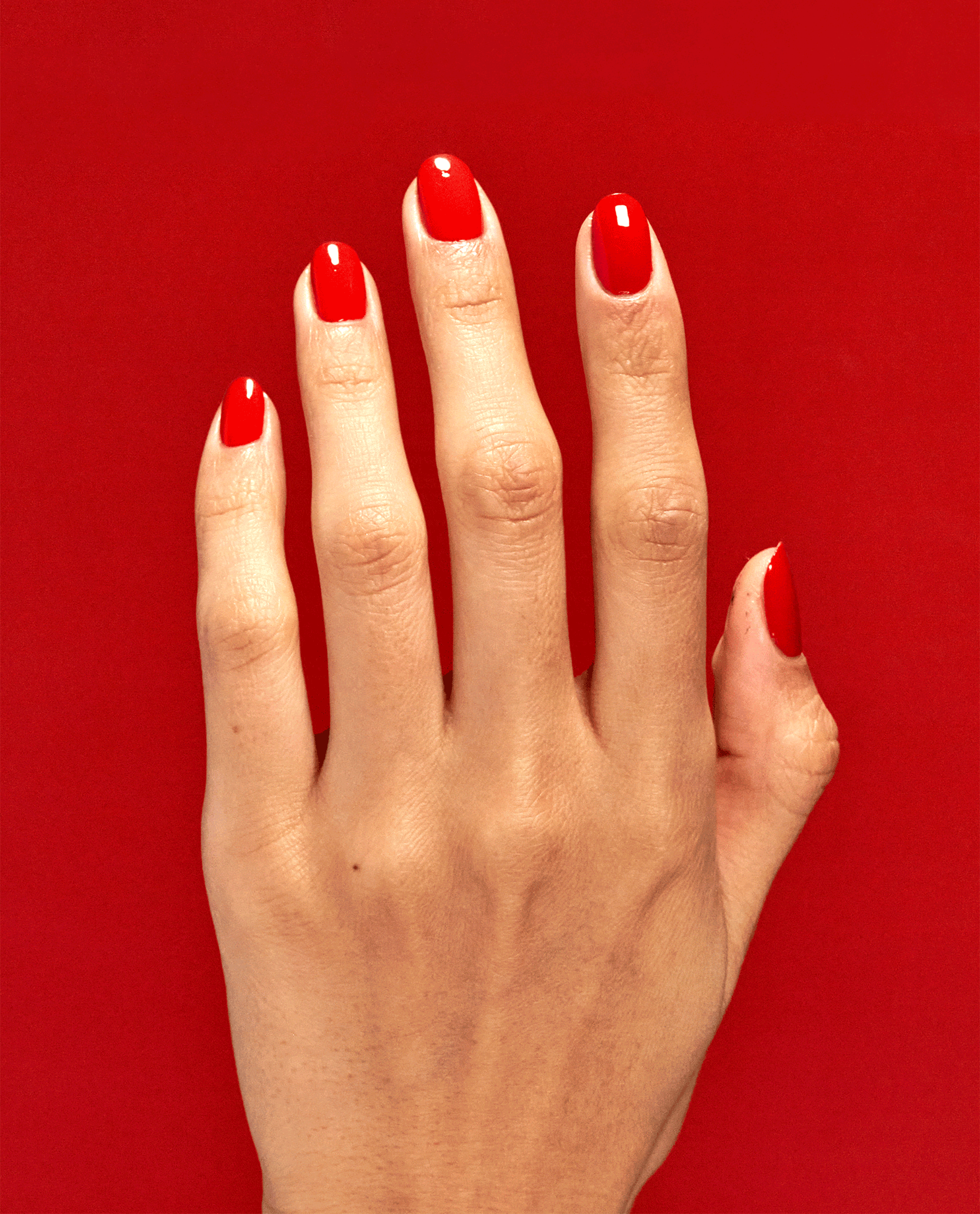 Hand with neatly manicured nails coated in Rust & Relaxation OPI nail polish, showing glossy rust-red nail lacquer against a matching bold red background, highlighting the rich color payoff and smooth salon-quality finish.
