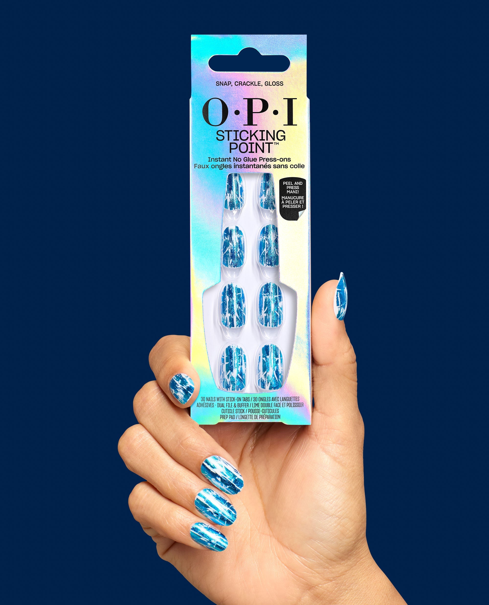 Hand holds OPI Snap, Crackle, Gloss Sticking Point press-on nails, a blue metallic crackle manicure option for fall nail colors, against a navy background.