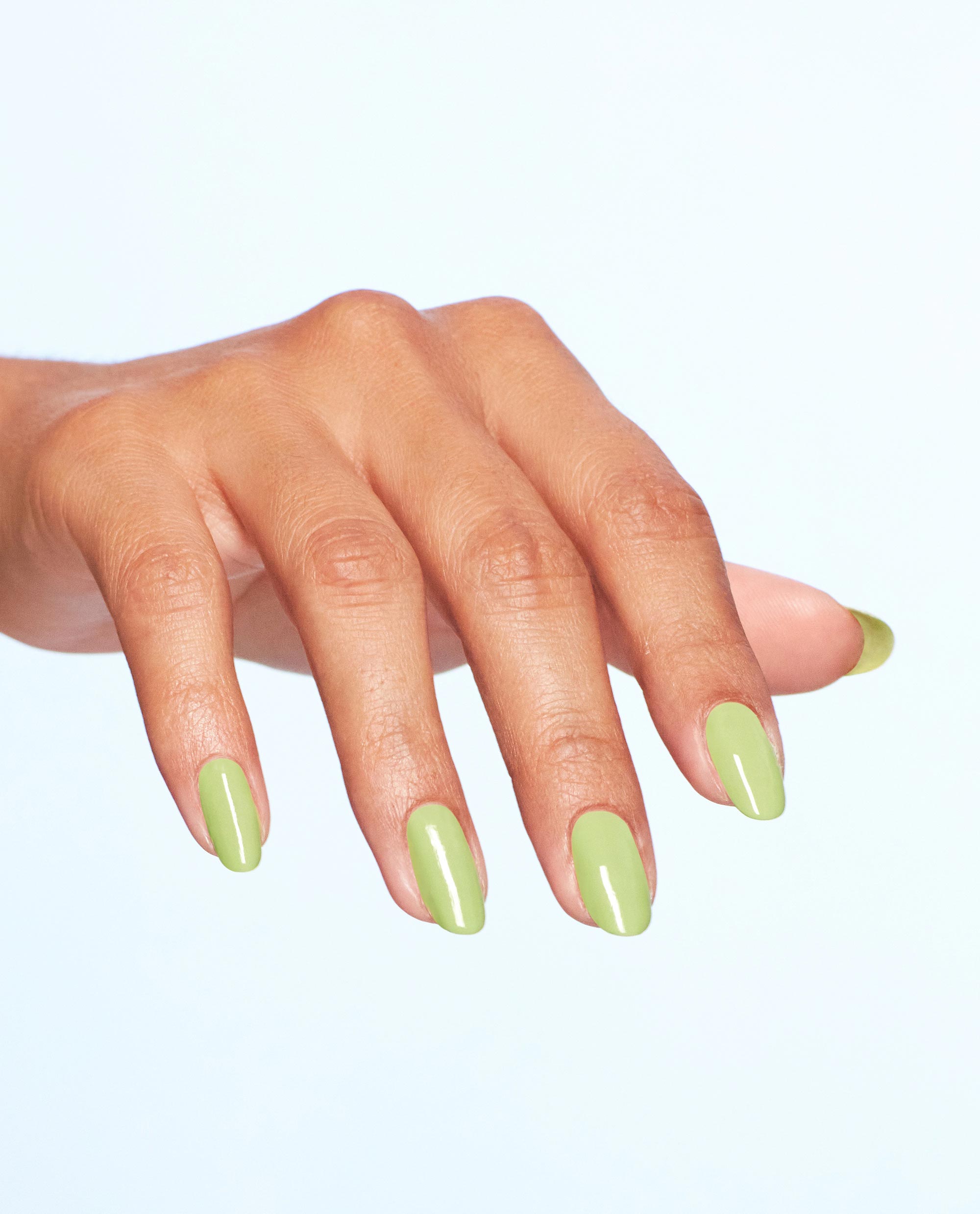Manicured hand showcases OPI Clear Your Cash dipping powder, a glossy pastel green nail polish, with almond-shaped nails spread against a clean light background, highlighting fresh spring nail colors.
