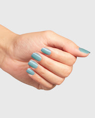 Manicured hand showcases Reality Check Ya Out Dipping Powder, a shimmery green nail polish shade, on short oval nails, gleaming under light against a plain gray background—fresh spring nail colors for OPI fans.