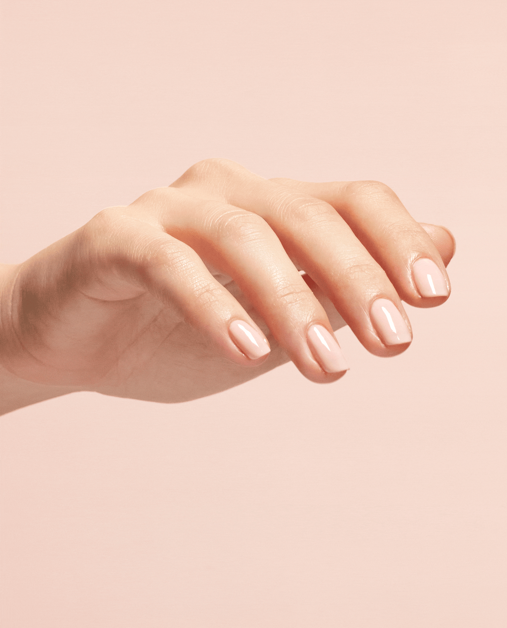 Hand with glossy natural-looking nails shows the smooth, high-shine finish created by OPI Start to Finish 3-in-1 Treatment top and base coat, styled against a soft pink background for a modern nail polish gift set product shot.