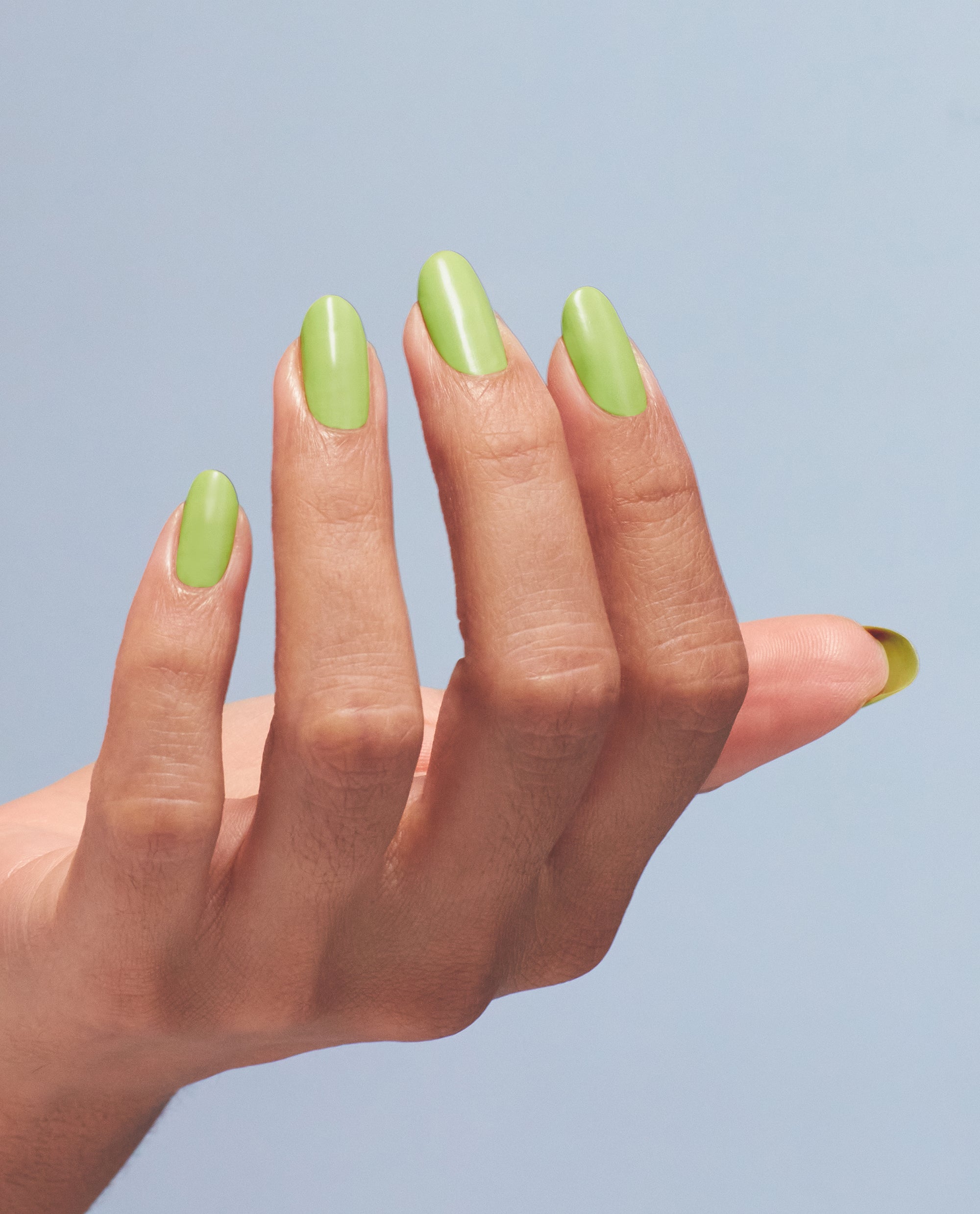 Manicured hand showcases glossy pastel‑lime nails painted with OPI Summer Monday-Fridays gel nail polish, a vibrant green nail polish perfect for spring nail colors, shown in close-up against a soft blue background.