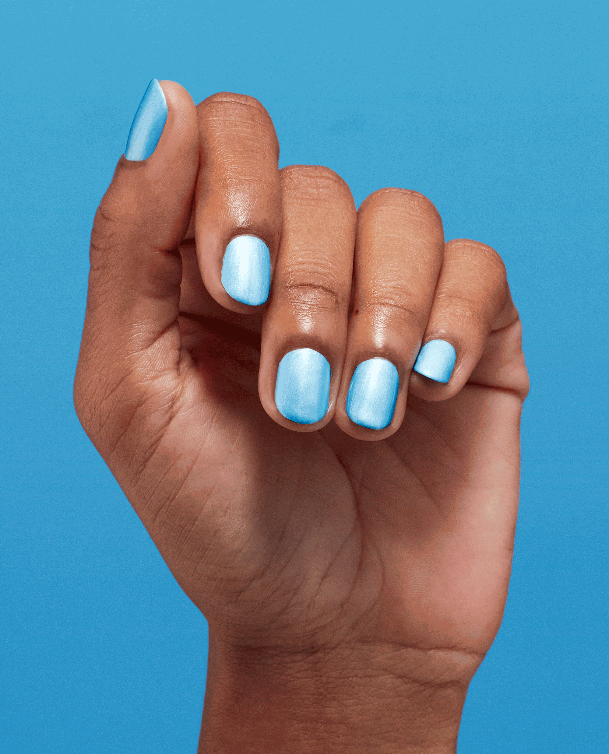 Hand poses with short nails painted Surf Naked nail lacquer, a glossy pale sky-blue shade against a bright blue background, showcasing OPI trending nail colors.