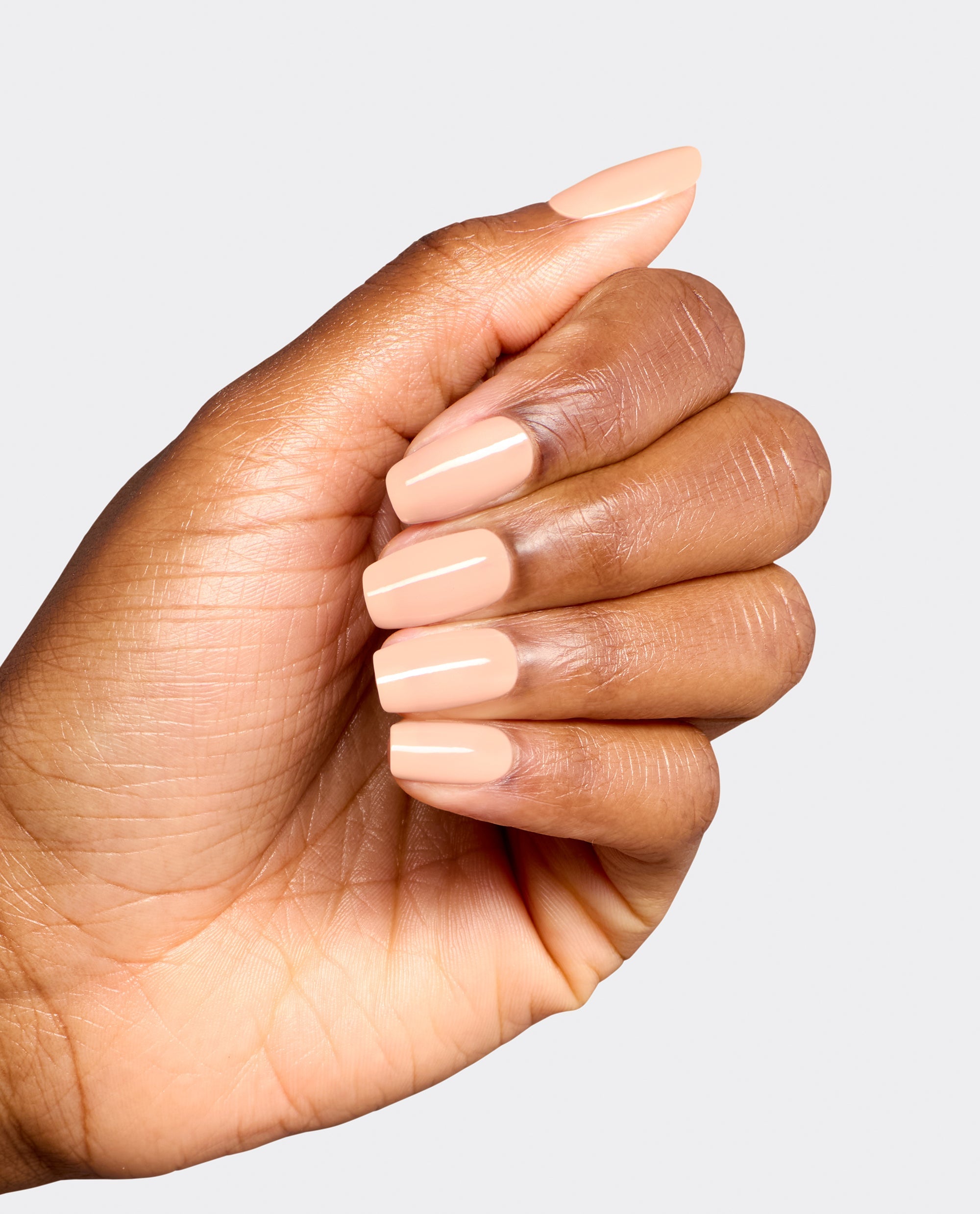 Hand modeling glossy, soft peach nude nails in OPI Suzi Take a Vow dipping powder, a subtle neutral shade for fall nail colors on a clean light gray background.