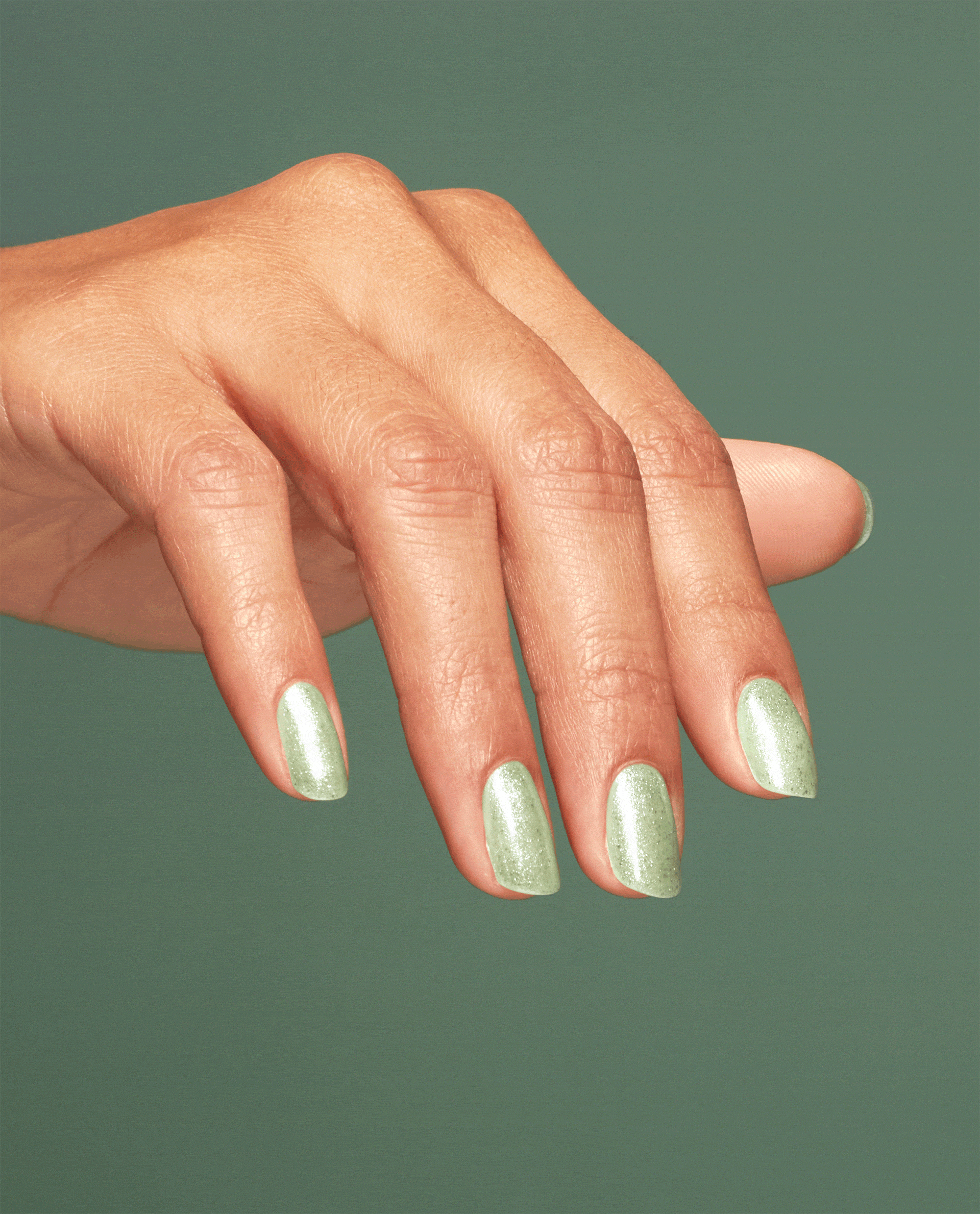 Hand with long almond-shaped nails shows off Taurus-t Me OPI nail polish, a shimmery light sage green nail lacquer, against a matching green background for a cohesive manicure beauty look.