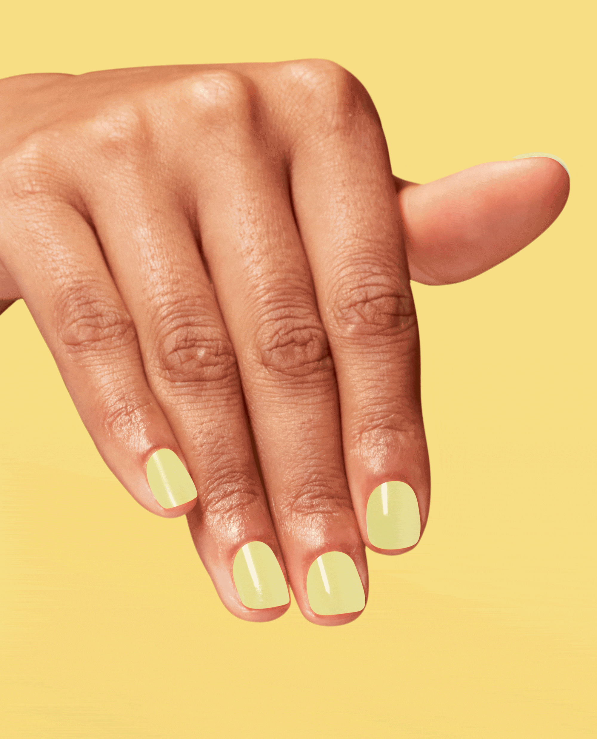 Hand modeling OPI Infinite Shine This Chic is Bananas, a glossy soft yellow nail polish, against a bright yellow background.
