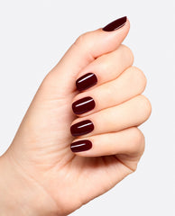 Hand displays glossy deep burgundy Vampire State Building dipping powder manicure with short rounded nails, an OPI-inspired fall nail color on a clean white background.