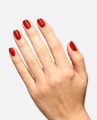Hand displays a glossy deep red OPI Vodka & Caviar dipping powder manicure on short rounded nails, showcasing classic fall nail colors against a light gray background.