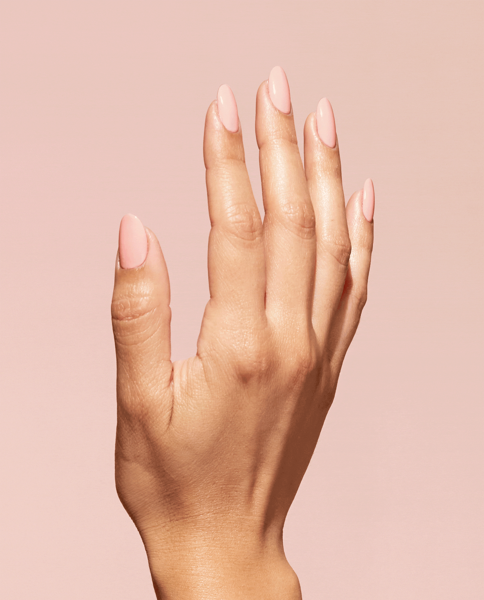 Hand with almond-shaped nails painted a glossy soft-peach shade, showcasing OPI We Canyon Do Better Nature Strong Vegan Nail Lacquer against a matching blush background, ideal hero shot for an OPI nail polish gift set product page.