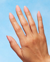 Hand with neatly manicured oval nails painted in OPI We Canyon Do Better, a soft peach-pink Nature Strong vegan nail lacquer, shown against a bright blue background for an OPI nail polish gift set product image.