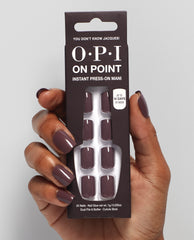 Hand with glossy taupe-mauve OPI On Point press-on nails holds the You Don’t Know Jacques! instant press-on mani box, showing matching nails and 14-day wear claim on a light gray studio background, ideal for fall nail colors.
