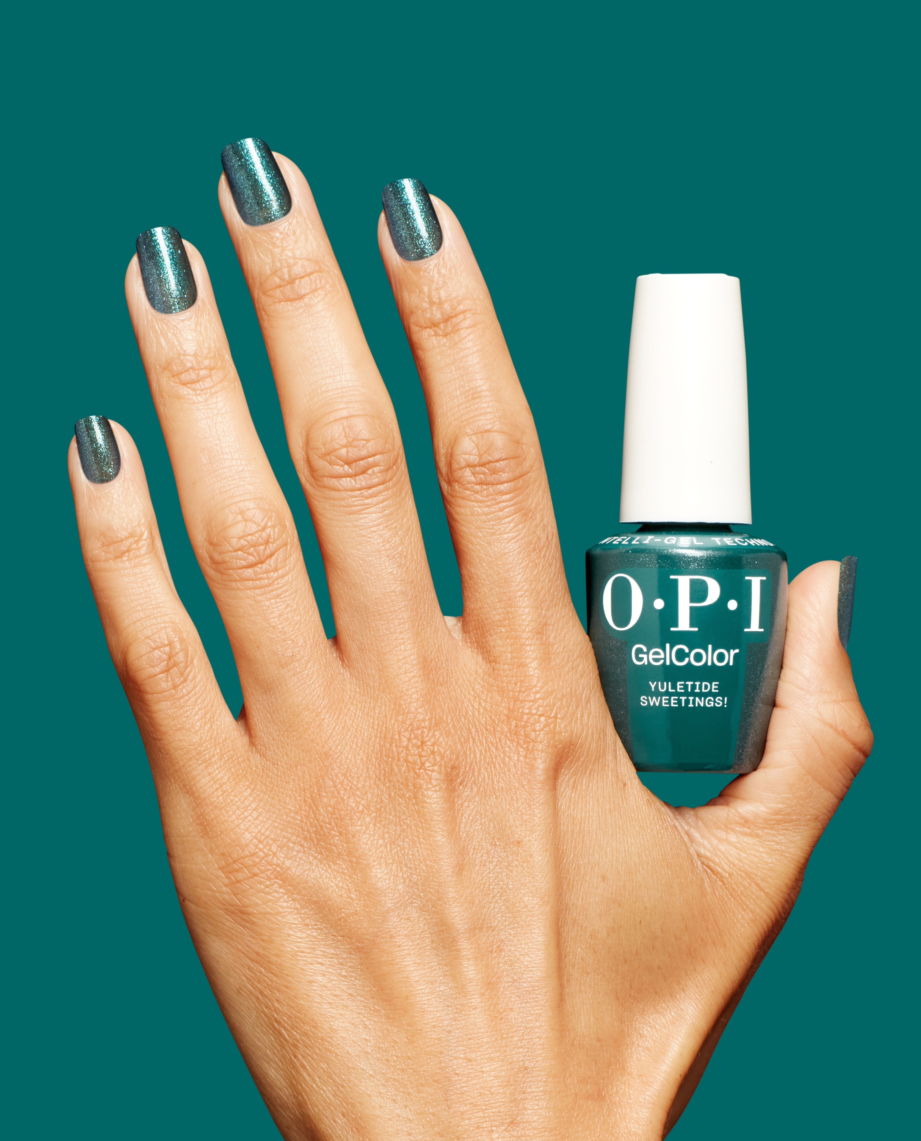 Manicured hand wearing shimmery deep teal green nail polish holds an OPI GelColor Yuletide Sweetings! gel nail polish bottle against a matching teal background, showcasing glossy sparkle; green nail polish pick for spring nail colors from OPI.