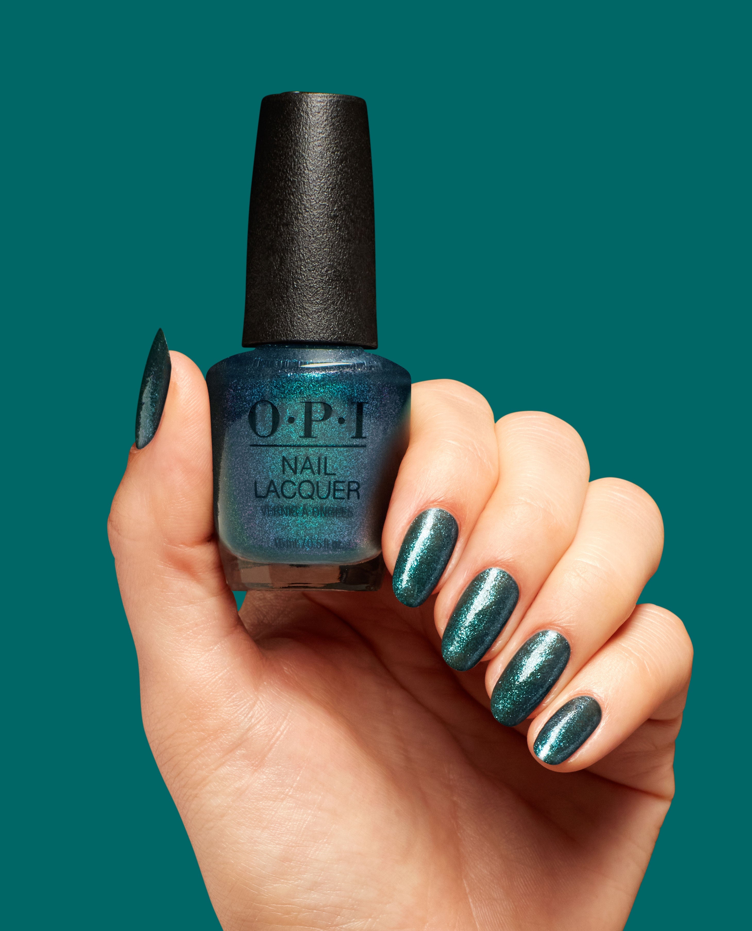 OPI Yuletide Sweetings! Nail Lacquer bottle held in a manicured hand, nails coated in a glossy shimmer deep teal-green to match, against a solid teal background—green nail polish by OPI, a bold pick for spring nail colors.
