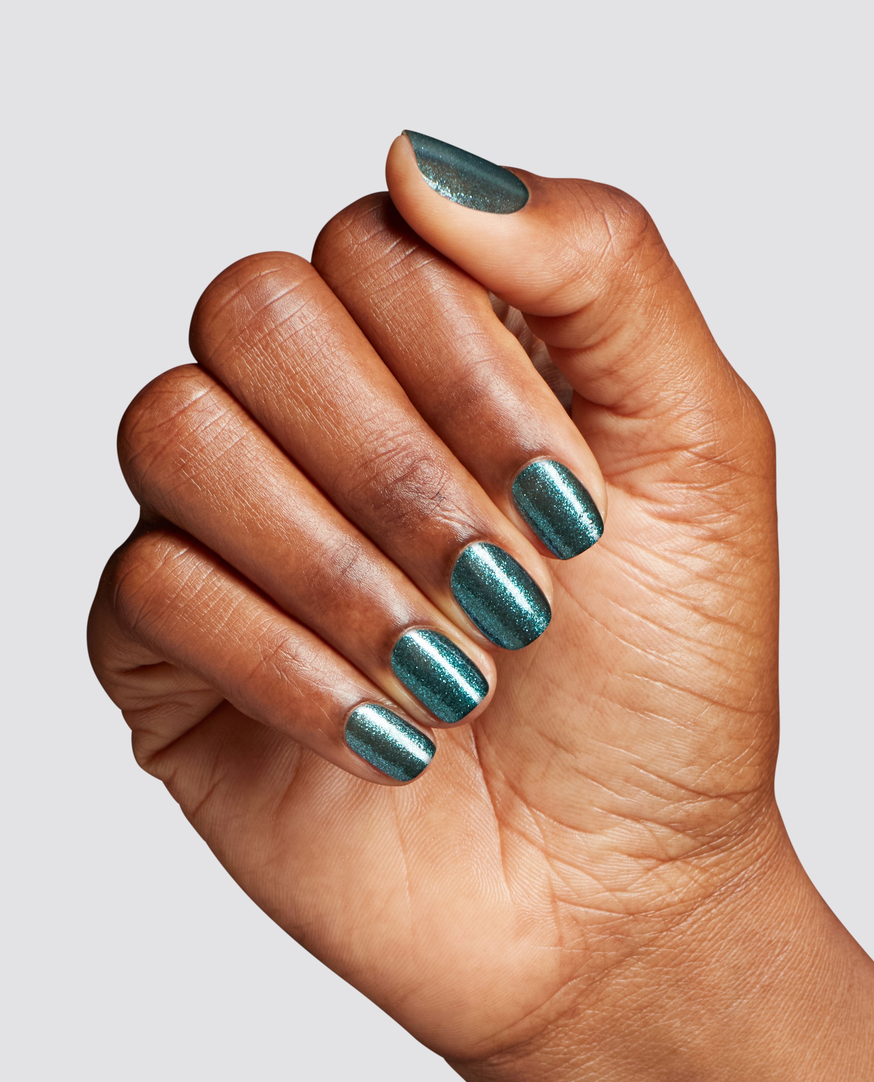 Manicured hand showcasing Yuletide Sweetings! nail lacquer by OPI, a shimmery deep green nail polish with fine glitter, catching light on short rounded nails against a clean gray background—glossy, festive color perfect for spring nail colors.